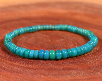 May include: A circular bracelet composed of small, disc-shaped beads in varying shades of turquoise, teal, and cyan. The beads are strung together in a continuous loop, featuring a smooth, polished finish with subtle variations in color intensity.