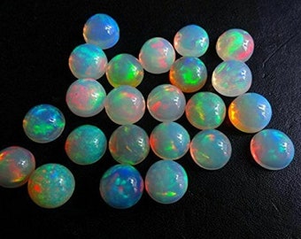 May include: A selection of round opal gemstones with a dark background. The opals exhibit a play of colour, with hues of blue, green, red, and yellow visible. Each stone has a unique pattern of iridescence.