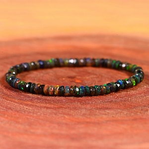 May include: A beaded bracelet made of small, faceted black opal stones. The bracelet shows a range of colours, including green, blue, and orange, and is set against a warm, reddish-brown background. The bracelet is approximately 18 cm in circumference.