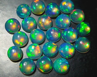 May include: A collection of 18 round, iridescent opal cabochons in various shades of blue, green, and yellow. The cabochons are smooth and polished, with a high gloss finish.