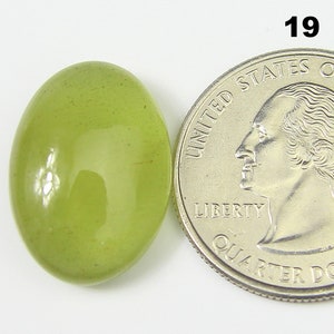 May include: A light green oval cabochon gemstone, approximately the size of a UK 20 pence coin. The stone has a smooth, polished surface and a translucent appearance.