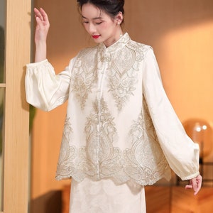 May include: A white sleeveless top with a gold embroidered design. The top has a mandarin collar and a button closure. The top is paired with a white skirt.