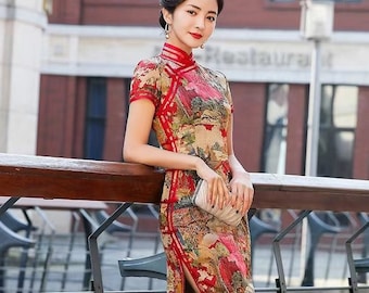 May include: A woman wearing a red and gold cheongsam with a floral print. The dress has a high collar and short sleeves. The woman is standing on a bridge and holding a white clutch.