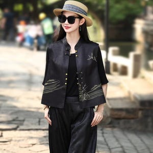 May include: A black outfit consisting of a vest, top, and pants. The vest has gold-colored buttons and embroidered landscape designs. The outfit is paired with a straw hat and sunglasses. The pants are loose-fitting.