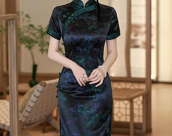 May include: A black satin cheongsam dress with a high collar and short sleeves. The dress features a green and blue floral pattern and green trim. The dress has a side slit and button details. The dress is a traditional Chinese garment.