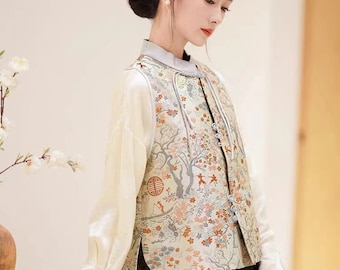May include: A woman wearing a white blouse with long sleeves and a cream-coloured waistcoat with a floral pattern. The waistcoat has a mandarin collar and a row of buttons down the front. The woman is also wearing a black skirt and carrying a brown handbag.