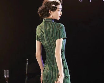May include: A woman wearing a green and gold striped cheongsam dress with a traditional Chinese fan. The fan is made of bamboo and has Chinese characters written on it.