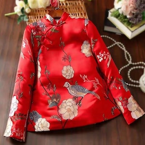 May include: A red silk blouse with a mandarin collar and floral embroidery. The blouse features a bird design and a traditional Chinese knot closure.