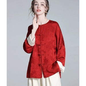 May include: A red silk blouse with a floral pattern and a mandarin collar. The blouse has a button closure and long sleeves with white cuffs.