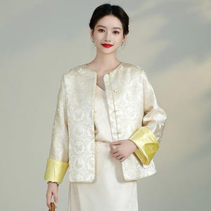 May include: A white jacket with a floral pattern and yellow cuffs. The jacket has a mandarin collar and a button closure.