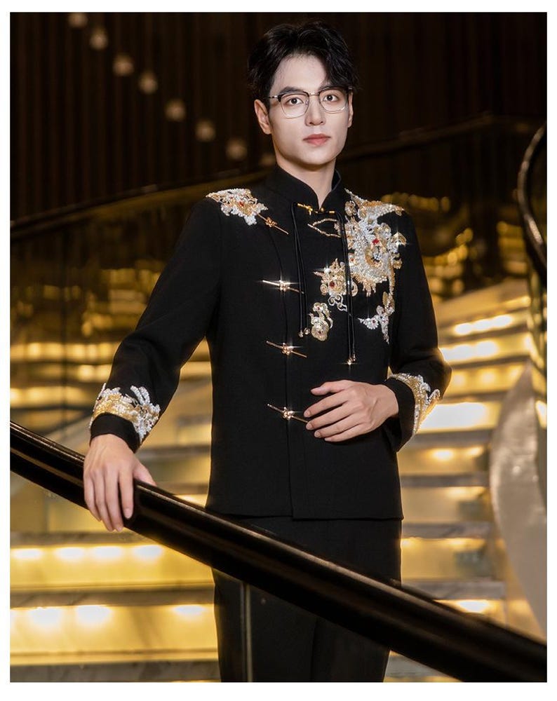May include: Black formal jacket with gold and white embroidery on the shoulders and sleeves. The jacket has a mandarin collar and decorative frog closures. The sleeves are long and the jacket is worn with black pants.