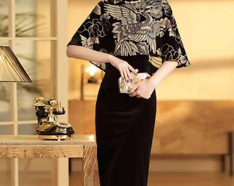 May include: A black velvet dress with a gold and black floral print cape. The dress has a mandarin collar and a fitted silhouette. The cape has a short, wide shape and is decorated with a large floral design.