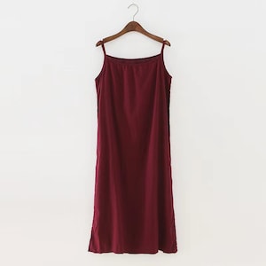 K&ouml;nnte beinhalten: Ein burgunderfarbenes, &auml;rmelloses Maxikleid mit d&uuml;nnen Tr&auml;gern, das an einem Holzb&uuml;gel h&auml;ngt.