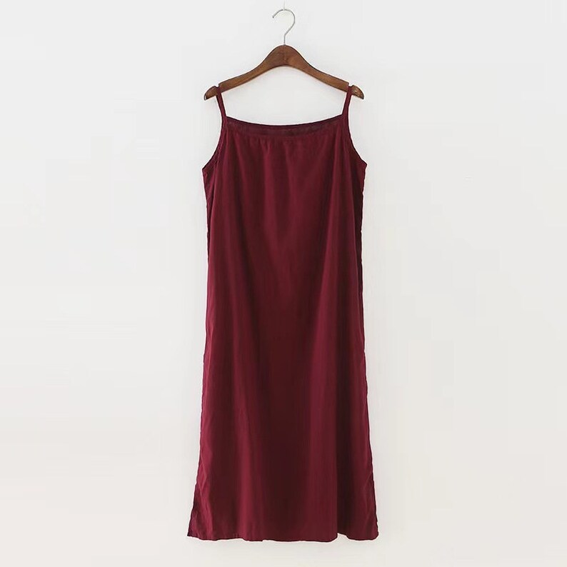K&ouml;nnte beinhalten: Ein burgunderfarbenes, &auml;rmelloses Maxikleid mit d&uuml;nnen Tr&auml;gern, das an einem Holzb&uuml;gel h&auml;ngt.