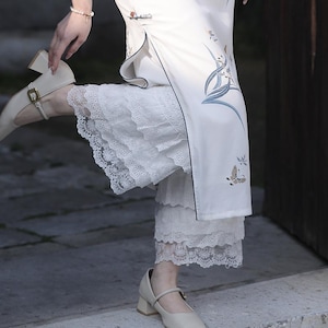 Könnte beinhalten: Weißer Spitzenunterrock mit mehreren Rüschenlagen. Der Unterrock wird unter einem weißen Kleid mit Blumenmuster getragen.