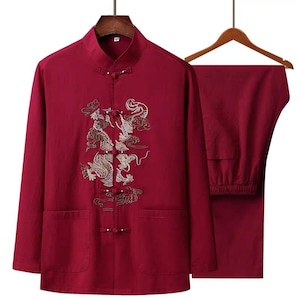 Puede incluir: Un conjunto tradicional chino de dos piezas en color burdeos. La parte superior de manga larga presenta un cuello mandarín, cierres de rana y dos bolsillos delanteros. Un bordado de dragón dorado adorna la parte delantera. Los pantalones a juego también son burdeos.