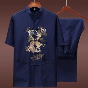 Puede incluir: Traje tradicional chino de dos piezas azul marino. La camisa de manga corta tiene cuello mandar&iacute;n, dos bolsillos delanteros y un dise&ntilde;o de drag&oacute;n dorado bordado. Los pantalones a juego tienen cintura el&aacute;stica. El conjunto est&aacute; en una percha de madera.
