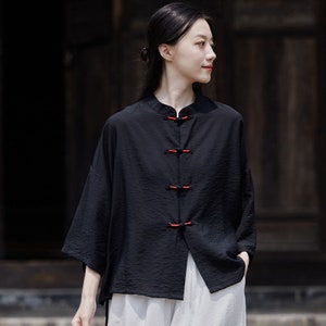 May include: A black, short-sleeved shirt with a mandarin collar and red buttons. The shirt is made of a lightweight fabric and has a relaxed fit.