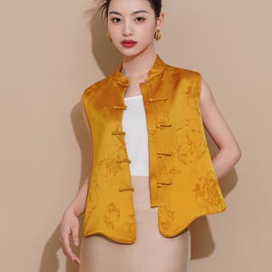 May include: A sleeveless yellow vest with a mandarin collar and floral pattern. The vest has a curved hemline and is fastened with decorative buttons.