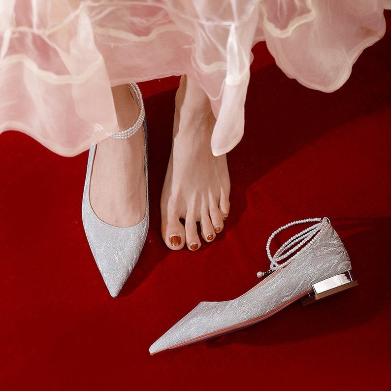 May include: A pair of silver sparkly pointed-toe flats with pearl embellishments. One shoe has a pearl ankle strap.