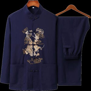 Puede incluir: Traje tradicional chino de dos piezas azul marino. La parte superior de manga larga presenta un cuello mandar&iacute;n y un dise&ntilde;o de drag&oacute;n bordado en oro en la parte delantera. Los pantalones a juego tienen cintura el&aacute;stica. El conjunto se muestra en una percha de madera.