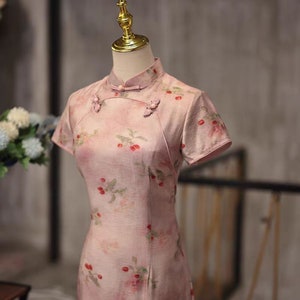 May include: A pink dress with a floral print and short sleeves. The dress has a mandarin collar and button closures.