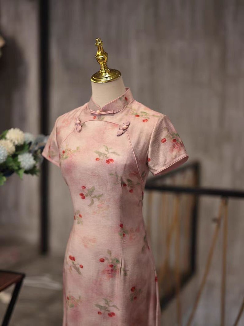 May include: A pink dress with a floral print and short sleeves. The dress has a mandarin collar and button closures.