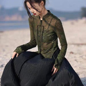 May include: An olive green blouse with a floral pattern and a mandarin collar, worn with a long, black skirt. The blouse has long sleeves. The outfit is suitable for a variety of occasions.