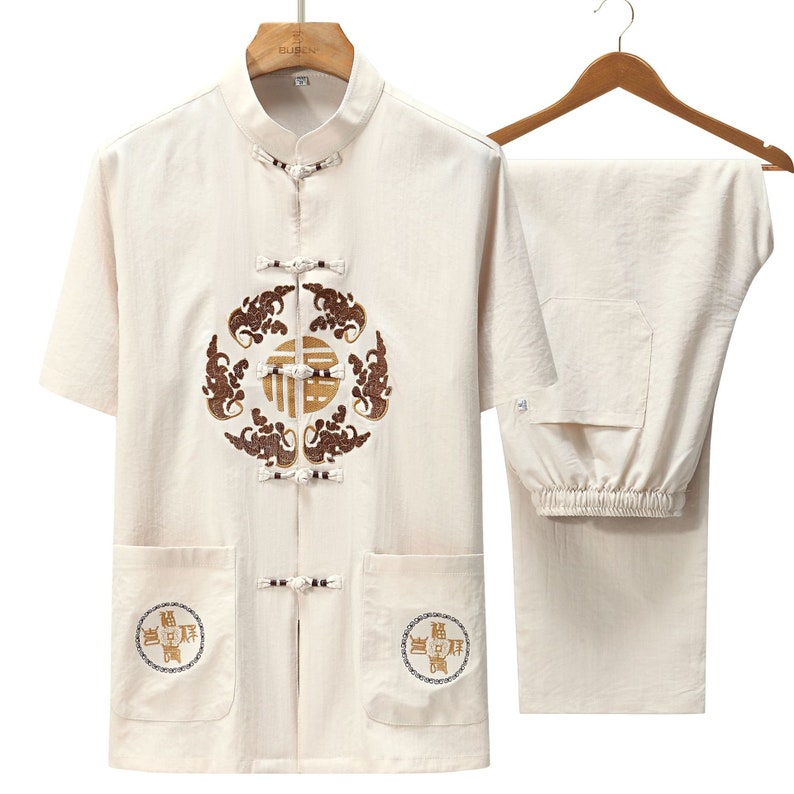 Puede incluir: Conjunto de dos piezas de lino color crema, que incluye una camisa de manga corta y un pantal&oacute;n a juego. La camisa presenta cuello mandar&iacute;n, cierres decorativos de rana y detalles bordados en marr&oacute;n y dorado. El pantal&oacute;n tiene cintura el&aacute;stica.
