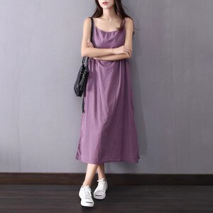K&ouml;nnte beinhalten: Ein langes, &auml;rmelloses, lila Maxikleid mit einem runden Ausschnitt. Das Kleid ist aus einem leichten Stoff gefertigt und hat eine lockere Passform. Das Model tr&auml;gt wei&szlig;e Sneaker.