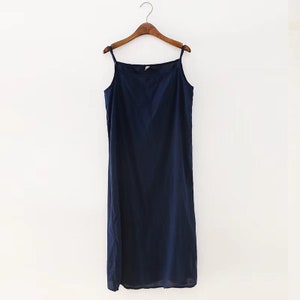 K&ouml;nnte beinhalten: Ein marineblaues, &auml;rmelloses Midikleid mit quadratischem Ausschnitt. Das Kleid h&auml;ngt an einem Holzb&uuml;gel.