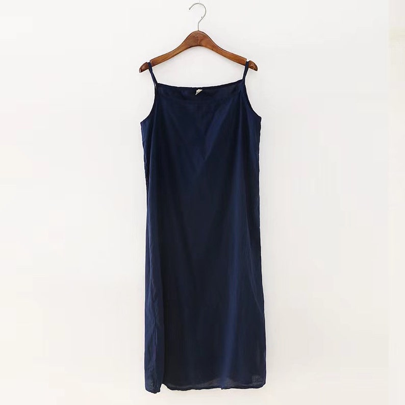 K&ouml;nnte beinhalten: Ein marineblaues, &auml;rmelloses Midikleid mit quadratischem Ausschnitt. Das Kleid h&auml;ngt an einem Holzb&uuml;gel.