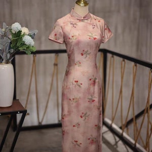 May include: A pink cheongsam dress with a floral print and short sleeves. The dress has a mandarin collar and a button closure at the neck.
