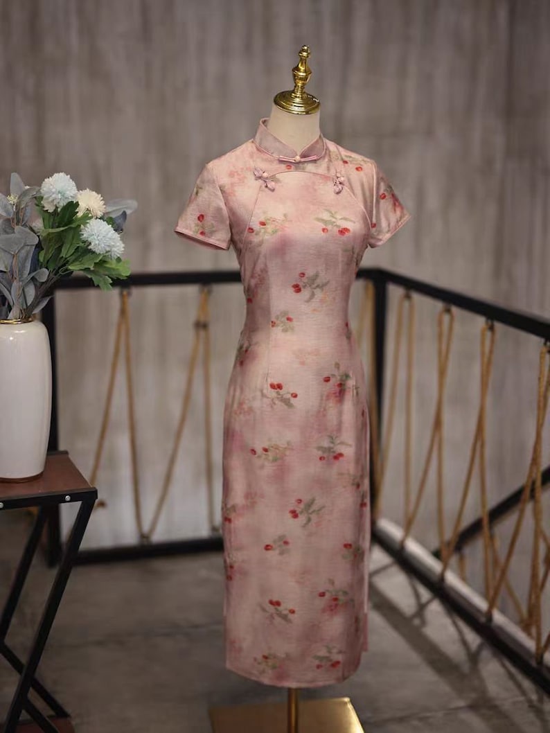 May include: A pink cheongsam dress with a floral print and short sleeves. The dress has a mandarin collar and a button closure at the neck.