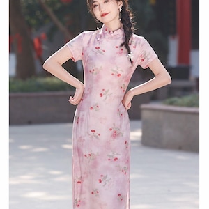May include: A pink and white floral print cheongsam dress with short sleeves and a mandarin collar. The dress has a fitted silhouette and a side slit.
