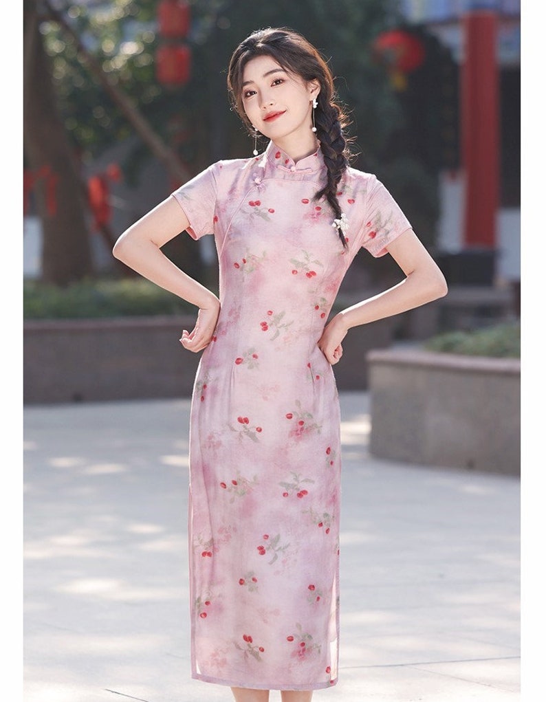 May include: A pink and white floral print cheongsam dress with short sleeves and a mandarin collar. The dress has a fitted silhouette and a side slit.