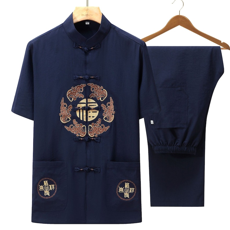 Puede incluir: Conjunto de ropa tradicional china de dos piezas azul marino. La camisa de manga corta presenta un dise&ntilde;o bordado en la parte delantera y dos bolsillos delanteros. Los pantalones a juego tambi&eacute;n son de color azul marino. El conjunto se muestra en una percha de madera.