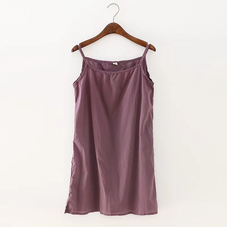 K&ouml;nnte beinhalten: Ein &auml;rmelloses, violettes, Baumwoll-Schlafkleid, das an einem Holzb&uuml;gel h&auml;ngt.
