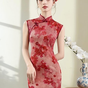 May include: A sleeveless red cheongsam dress with a floral print. The dress has a mandarin collar and a button closure. The dress is fitted and has a knee-length hem.