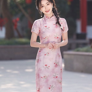 May include: A woman wearing a pink and white floral dress with a mandarin collar. The dress has a cherry print and is knee-length.