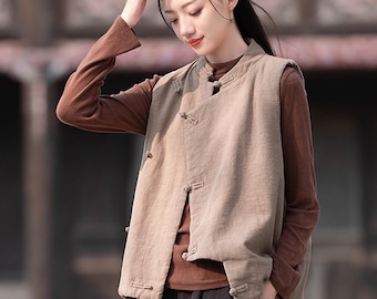 May include: A woman wearing a brown sleeveless top with a mandarin collar and a brown long-sleeved shirt underneath. She is wearing black pants and has her hair pulled back.