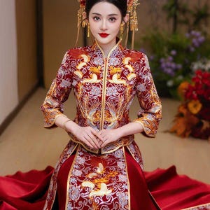 Könnte beinhalten: Eine Frau in einem traditionellen chinesischen Hochzeitskleid mit aufwendigen goldenen Stickereien auf rotem Grund. Das Kleid besteht aus einem langen Rock und einem taillierten Oberteil mit hohem Kragen. Sie trägt ein goldenes Kopfstück mit herabhängenden Ornamenten.