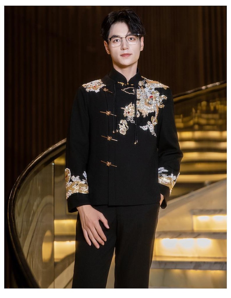May include: Black formal jacket with ornate gold and white embroidery, featuring a dragon design on the front and sleeves. The jacket has a mandarin collar and gold frog closures. The person is wearing black pants and glasses.