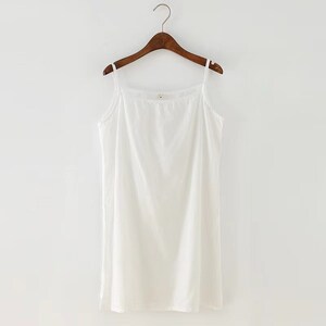 K&ouml;nnte beinhalten: Ein wei&szlig;es &auml;rmelloses Tanktop mit einem runden Ausschnitt, das an einem Holzb&uuml;gel vor wei&szlig;em Hintergrund h&auml;ngt.
