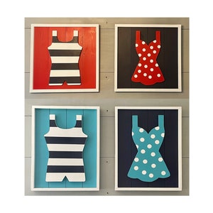 May include: Four framed wood signs with different colored backgrounds and cutout images of swimwear. The top left sign has a red background with a black and white striped swimsuit. The top right sign has a black background with a red and white polka dot swimsuit. The bottom left sign has a blue background with a black and white striped swimsuit. The bottom right sign has a dark blue background with a turquoise and white polka dot swimsuit.