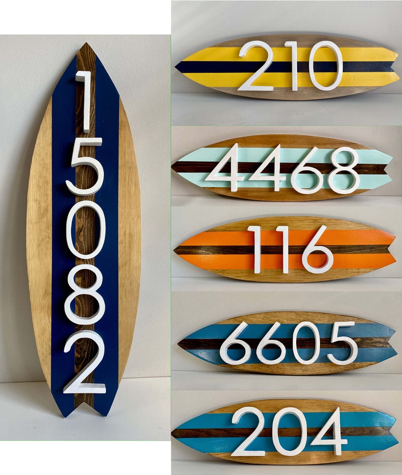 Puede incluir: Cinco letreros de n&uacute;meros de casa de madera con forma de tabla de surf con rayas de colores diferentes y n&uacute;meros blancos. Los n&uacute;meros son 210, 4468, 116, 6605 y 204.
