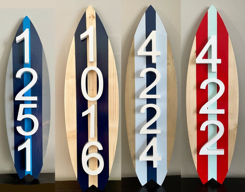 Puede incluir: Tres letreros de n&uacute;meros de casa de madera con forma de tabla de surf con n&uacute;meros blancos. El primer letrero es azul y gris con los n&uacute;meros 1251. El segundo letrero es de madera con rayas azules y blancas y los n&uacute;meros 1016. El tercer letrero es rojo y blanco con los n&uacute;meros 4224.