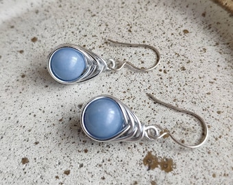 May include: A pair of silver wire wrapped earrings with light blue gemstone beads.