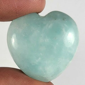 May include: A heart-shaped aquamarine crystal with a light blue and white color. The crystal is smooth and polished.