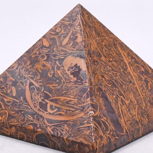 May include: A pyramid-shaped decorative object made of brown stone with intricate patterns in shades of orange and dark brown. The pyramid has a square base and a pointed top, showcasing a natural, earthy aesthetic.